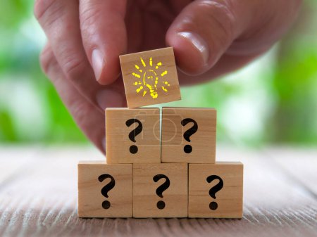 Photo for Hand placing wooden cube with yellow color light bulb on top of other cubes with question mark. Idea concept. - Royalty Free Image