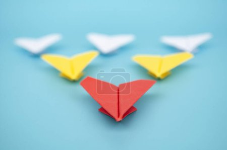 Téléchargez les photos : Vue rapprochée de l'origami de l'avion en papier rouge menant avions en papier jaune et blanc sur fond de couverture bleue. - en image libre de droit