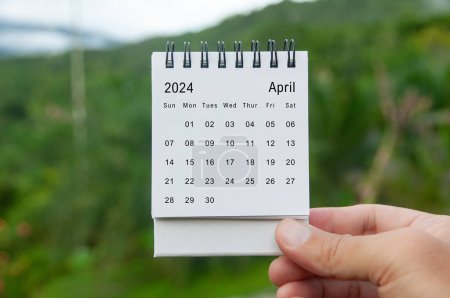 Hand hält April 2024 weißen Kalender mit Naturhintergrund. Feiertags- und Kalenderkonzept.