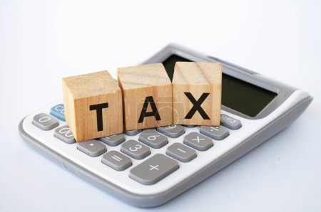 Steuerliche Formulierungen auf Holzwürfeln auf weißem Einband-Hintergrund mit Taschenrechner-Hintergrund. Steuerkonzept.