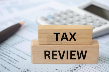 Tax review text on wooden blocks with tax form and calculator background. Taxation concept.