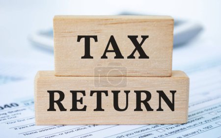 Text der Steuererklärung auf Holzklötzen mit Steuerformular und Taschenrechnerhintergrund. Steuerkonzept.