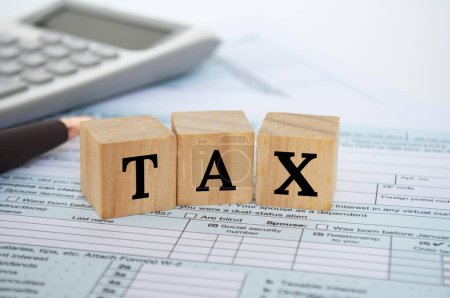 Steuerliche Formulierungen auf Holzwürfeln mit Steuerformular und Taschenrechnerhintergrund. Steuerkonzept.