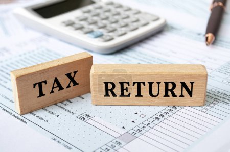 Text der Steuererklärung auf Holzklötzen mit Steuerformular und Taschenrechnerhintergrund. Steuerkonzept.
