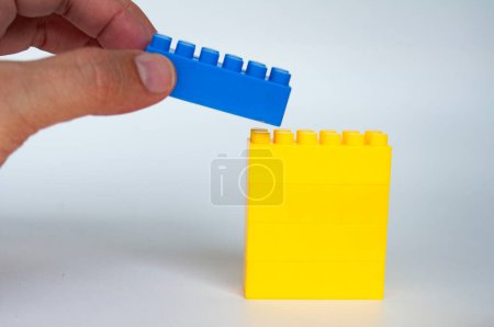 Mano apilando lego de color azul en otro conjunto de lego. Concepto de construcción.