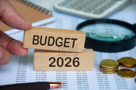Hand hält Holzblock mit Text - Haushalt 2026 mit Finanzdaten Hintergrund. Haushaltskonzept