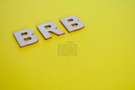 BRB wooden letters representing Be Right Back on yellow background.