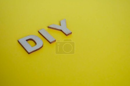 DIY wooden letters representing Do It Yourself on yellow background.