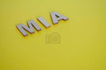 Foto de Letras de madera MIA que representan Missing In Action sobre fondo amarillo. - Imagen libre de derechos