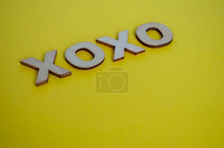 XOXO Holzbuchstaben, die Umarmungen und Küsse auf gelbem Hintergrund darstellen.