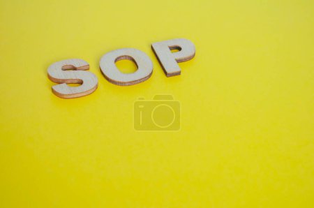 Lettres SOP en bois représentant les procédures opératoires normalisées sur fond jaune.