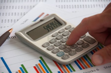 Hand pressing calculator with financial analysis paper. Business strategy and budget concept.