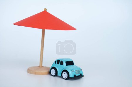 Red toy umbrella and blue toy car on white background.