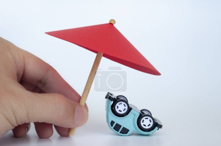 Red toy umbrella and upside down blue toy car on white background.