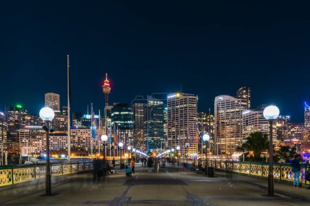 Foto de Sydney, Australia - April 16, 2022: Illuminated Sydney City skyline viewed from Pyrmont Bridge through Darling Harbour at night time - Imagen libre de derechos