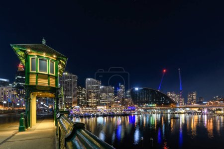 Foto de Sydney, Australia - 16 de abril de 2022: El horizonte iluminado de la ciudad de Sydney visto desde el puente Pyrmont a través de Darling Harbour por la noche - Imagen libre de derechos