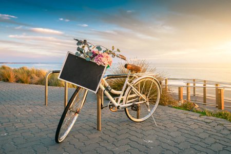 Oldtimer-Fahrrad mit Textrahmen auf einem Lenkrad, das bei Sonnenuntergang in Strandnähe abgestellt ist
