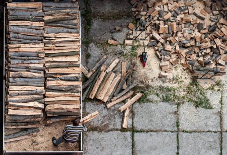 Ein Unbekannter entlädt Brennholz aus einem LKW. Kettensäge, die in einem Hinterhof von abgesägten Baumstämmen abgestellt wurde. Aus der Vogelperspektive.