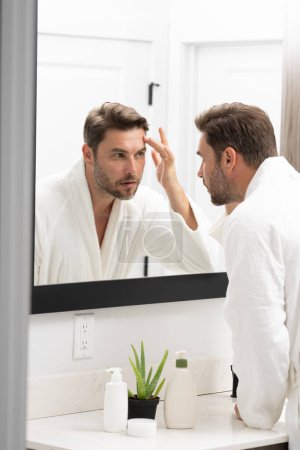 Young happy manful guy applying face cream. Close up shot of attractive man with healthy skin, applies cream for anti wrinkle or anti aging, cares of body. Beauty portrait. Body positive. Skin