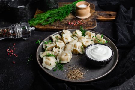 Téléchargez les photos : Dumplings à la crème sure et aux herbes sur une assiette sombre. Boulettes de viande - en image libre de droit