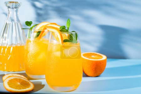 Téléchargez les photos : Jus d'orange frais avec glace dans un verre sur fond bleu. cocktail orange - en image libre de droit