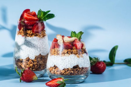 Téléchargez les photos : Granola avec yaourt, chia et fraises dans un verre sur un fond lumineux - en image libre de droit