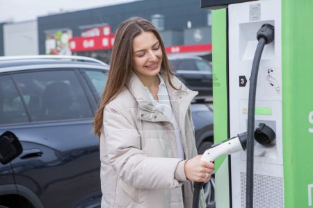 Young woman charging her electric car at a charging station in the city. Eco fuel concept. The concept of environmentally friendly transport. Recharging battery from charging station.
