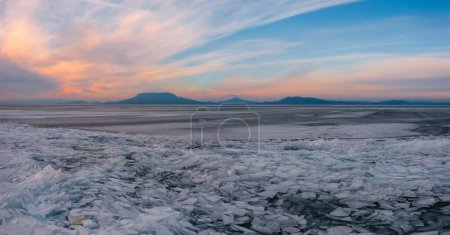 Photo for Fonyod, Hungary - Aerial view about frozen lake Balaton with Badacsony and Gulacs at the background. Stunning cloudy winter sunset. - Royalty Free Image