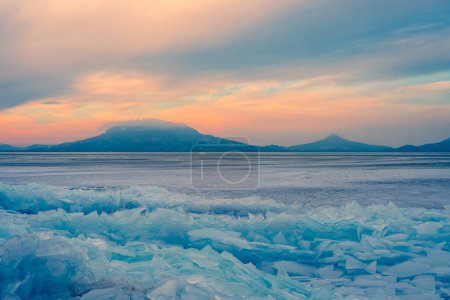 Téléchargez les photos : Fonyod, Hongrie - Beaux icebergs sur la rive du Balaton gelé. Badacsony et Gulacs avec un spectaculaire coucher de soleil nuageux en arrière-plan. - en image libre de droit