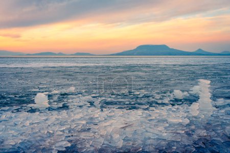 Photo for Fonyod, Hungary - Beautiful icebergs on the shore of the frozen Balaton. Badacsony and Gulacs with a spectacular cloudy sunset in the background. Winter landscape. - Royalty Free Image