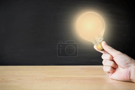 Foto de Man hold Light bulb on the wood table with black background. Knowledge education and Infinite Learning concept. - Imagen libre de derechos