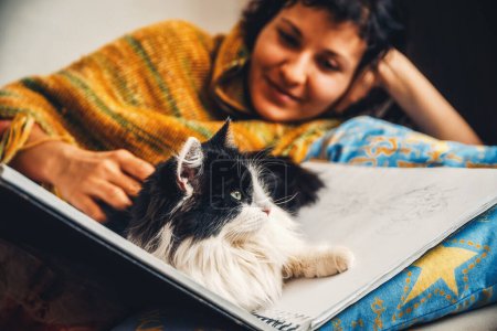 Téléchargez les photos : Sérénissime et captivante, une femme s'incline sur un lit, accompagnée d'un chat noir et blanc. - en image libre de droit