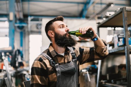 Ein Arbeiter trinkt in einer Pause Bier in einer Fabrik.