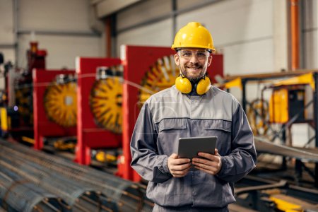 Porträt eines Metallurgiearbeiters mit Tablet in der Anlage, während er in die Kamera lächelt.