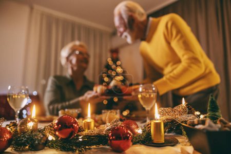 Focus sélectif sur un ornements de Noël et des bougies sur la table de Noël et la veille du Nouvel An avec un couple de personnes âgées floues.