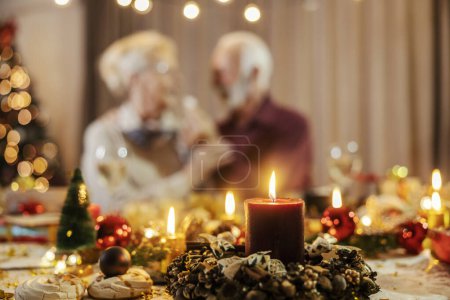 Close up of candle and christmas decorations on a table on christmas and new year's eve with a senior couple in a blurry background.