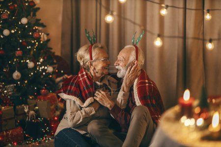 Una pareja de ancianos festivos está celebrando la Navidad y el año nuevo en casa acogedora mientras se abraza.