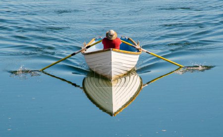 Photo for Man in a rowboat with reflection on calm water - Royalty Free Image