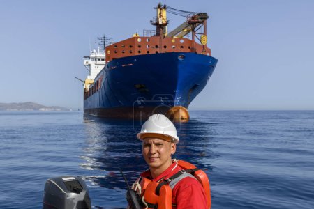 Orangefarbenes Rettungsboot mit Besatzung auf See mit großem blauem Frachtschiff im Hintergrund. Der Mensch über Bord. Rettungsbootausbildung.