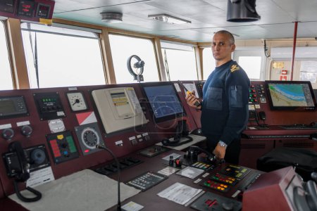 Offizier mit Funkgerät auf der Schiffsbrücke. Kaukasier im blauen Uniformpullover auf der Brücke eines Frachtschiffs.