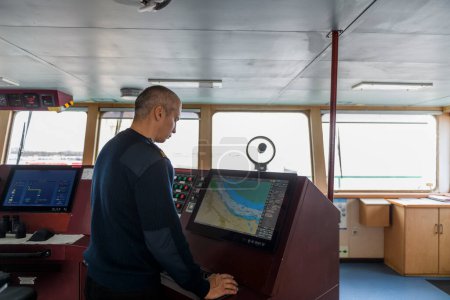 Offizier auf Wache mit elektronischer Karte auf der Schiffsbrücke. Kaukasischer Mann in blauem Uniformpullover mit ECDIS auf der Brücke eines Frachtschiffs.
