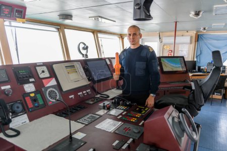 Offizier auf Wache mit SART auf der Schiffsbrücke. Kaukasischer Mann in blauem Uniformpullover mit Such- und Rettungs-Radartransponder auf der Brücke des Frachtschiffs.