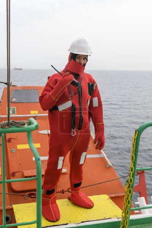 Seaman wearing Immersion Suit on Muster station. Abandon ship drill. Free fall boat. Cargo vessel.