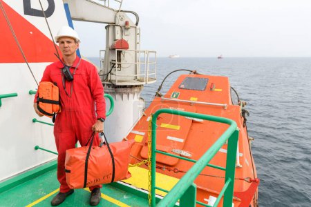 Seaman wearing lifejacket with vhf radio on Muster station. Abandon ship drill. Free fall boat. Cargo vessel.
