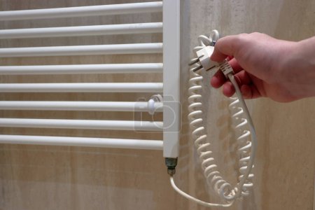 Téléchargez les photos : Electric heating switched off. A hand holds an electric plug. Heated ladder for towels. - en image libre de droit
