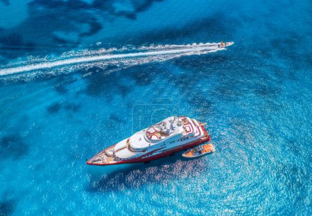 Téléchargez les photos : Vue aérienne du magnifique yacht de luxe rouge et du bateau en mer bleue au coucher du soleil en été. Sardaigne, Italie. Vue de dessus du bateau de vitesse, côte de la mer, eau transparente. Voyage. Paysage tropical. Yachting - en image libre de droit