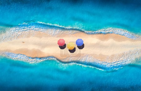 Téléchargez les photos : Aerial view of transparent blue sea with waves on the both sides and sandy beach with colorful umbrellas at sunset. Top view of sandbank. Summer travel. Tropical landscape with white sand and ocean - en image libre de droit