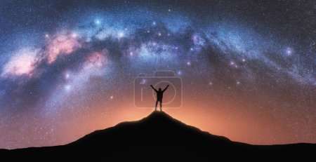 Téléchargez les photos : Voie lactée et homme heureux au sommet de la montagne la nuit étoilée. Silhouette de type avec bras levé sur la colline, ciel étoilé, lumière jaune au Népal. Galaxie. Paysage spatial avec voûte laiteuse - en image libre de droit