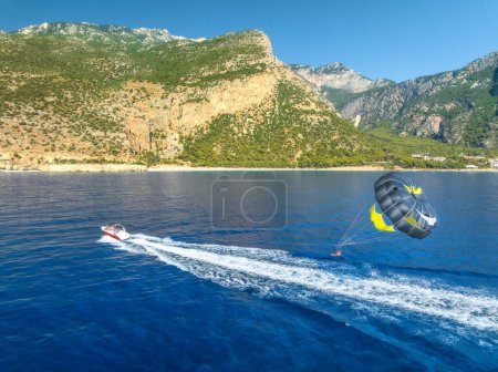 Photo for Aerial view of parasailing on the blue sea in Oludeniz, Turkey. Top view of speed boat, water and people with parasail, mountains, beach at sunset in summer. Extreme vacation. Sport. Travel - Royalty Free Image