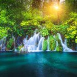 Waterfall in green forest in Plitvice Lakes, Croatia at sunset in summer. Colorful landscape with fall, blooming park, trees, water lilies, river in spring. Scenery. Park in woods at dusk. Nature